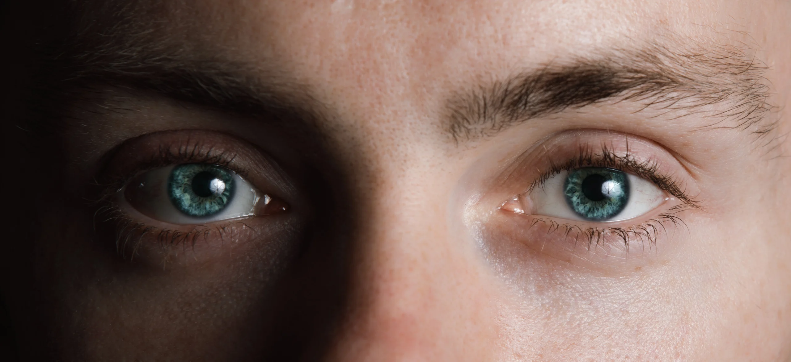 A close up of a man's blue eyes, his face is half in shadow.